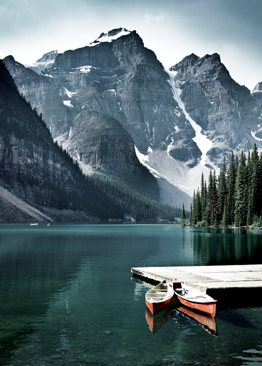  – Fotografía de dos canoas color rojo en el muelle pequeño de un lago con montañas altas al fondo y bosque