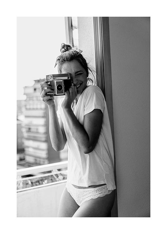 Fotografía en blanco y negro de una mujer sonriendo mientras sostiene una cámara y lleva una camiseta blanca
