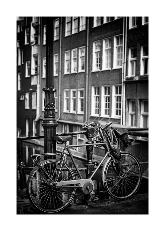  - Fotografía en blanco y negro de una bicicleta junto a una farola, frente a un edificio con ventanas. 