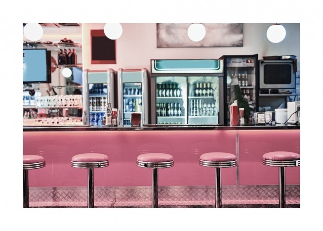  - Fotografía de una cafetería vintage con banquetas de bar junto a un mostrador rosa. 
