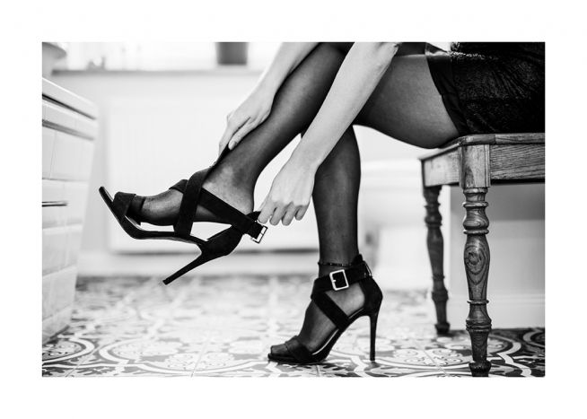  – Fotografía en blanco y negro de una mujer sentada en una silla poniéndose sus tacones.