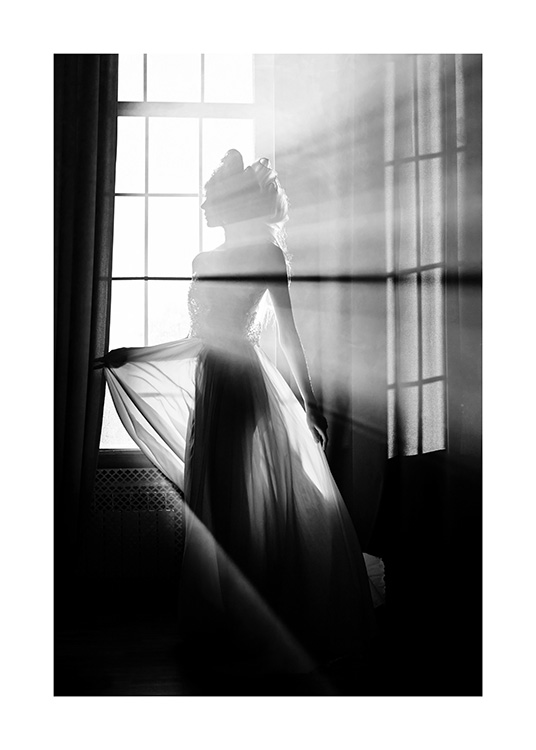  - Fotografía en blanco y negro de una joven que lleva un vestido insinuante y transparente y está frente a una ventana iluminada por los rayos de sol. 