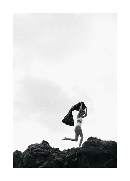  - Fotografía artística en blanco y negro de una mujer que lleva un bikini blanco y va corriendo sobre unas rocas con una toalla sobre la cabeza.