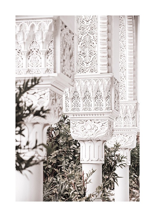  - Primer plano de unas columnas blancas con detalles artesanales y hojas verdes en el fondo.