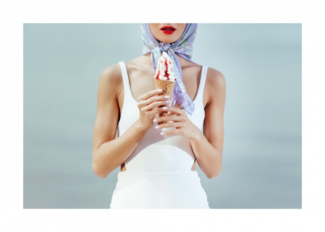  – Fotografía estilo vintage de una mujer frente al mar Lleva un traje de baño banco y una pañuelo azul en la cabeza, y tiene un helado de crema en la mano