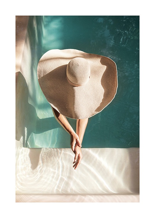  – Fotografía de una mujer con un sobrero de sol grande, de pie en una piscina y con los brazos estirados.