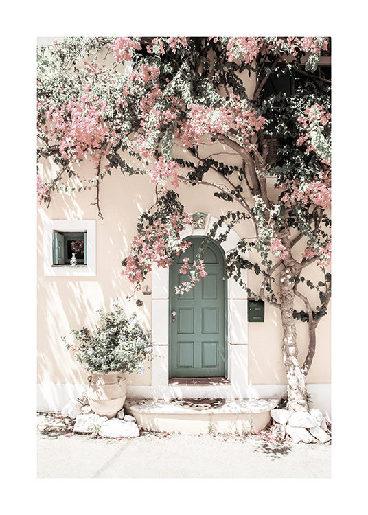 – Fotografía de la fachada de una casa con una puerta verde y un árbol de flores rosas.