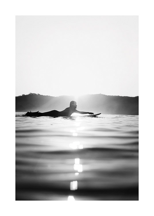  – Fotografía en blanco y negro con una persona remando sobre su tabla de surf.