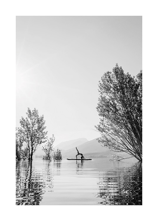  – Fotografía en blanco y negro de una mujer practicando una pose de yoga sobre una tabla de surf en medio de un lago.