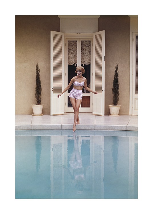  – Fotografía de una mujer que está mojándose los pies en una piscina y lleva un bikini de estilo vintage a cuadros rosas y blancos.