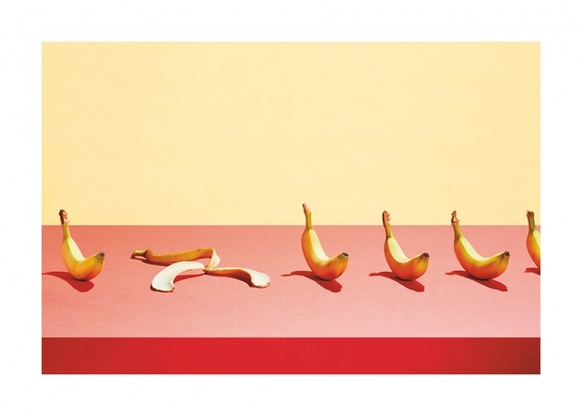  – Fotografía de una hilera de plátanos sobre una mesa rosada y pared amarilla.