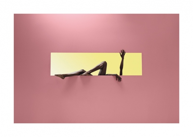  – Fotografía de una mujer que estira las piernas y los brazos a través de la apertura de un rectángulo ubicado en una pared rosa