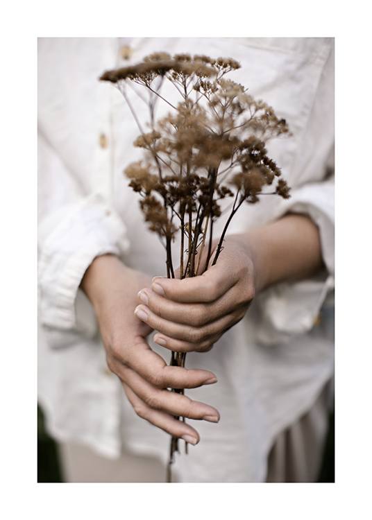  – Fotografía de una mujer con camisa blanca de lino que sostiene un ramillete de flores secas.
