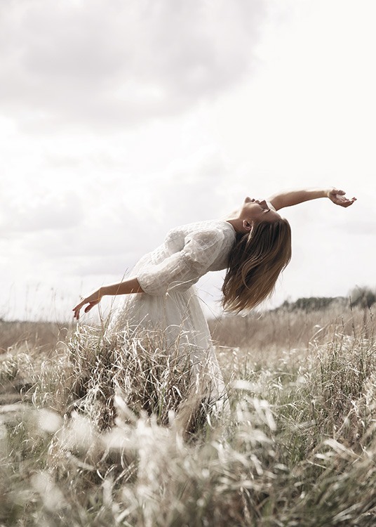  – Fotografía de una mujer con vestido blanco haciendo una pose en un campo de pastos altos.