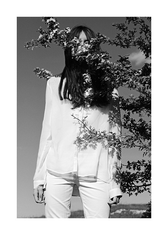  – Fotografía en blanco y negro de una mujer vestida de blanco y unas ramas en flor que le cubren el rostro