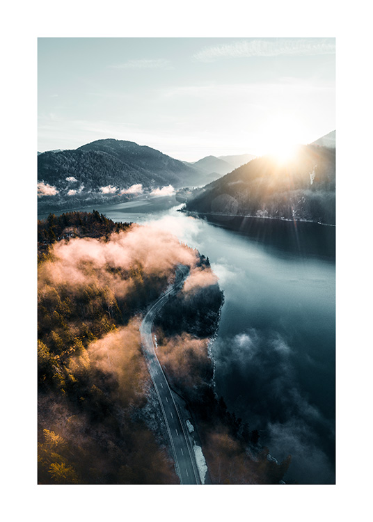  – Fotografía aérea de un camino entre un lago y un bosque, con montañas bañadas por el sol
