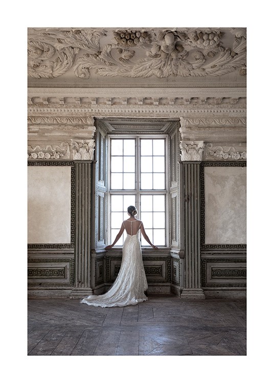  – Fotografía de una mujer con un vestido largo blanco de pie frente a una ventana