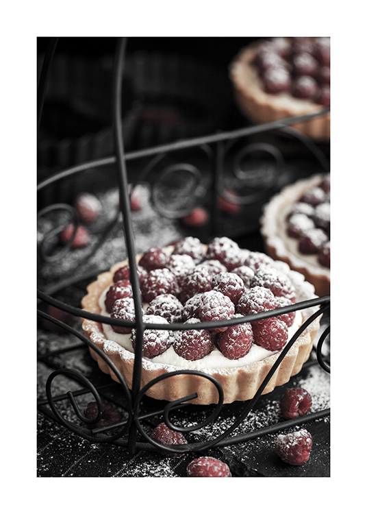  – Fotografía de unos pasteles con frambuesas y azúcar glasé colocadas en una bandeja negra de metal con decoraciones