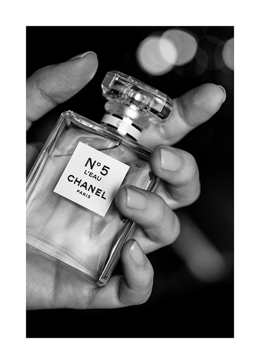  – Fotografía en blanco y negro de una mano que sostiene un frasco de perfume Chanel No5
