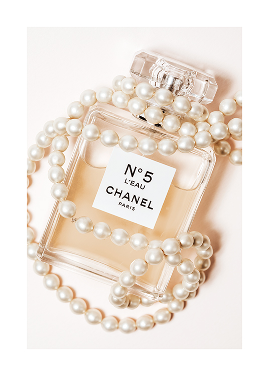  – Fotografía de un frasco de perfume Chanel No5 con un collar de perlas, fondo beis claro