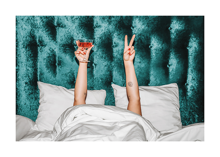  – Mujer con una copa naranja en una cama con cabecero de terciopelo turquesa