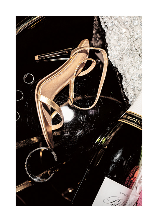  – Fotografía de un champán, tacones dorados, joyas plateadas y un vestido con lentejuelas.