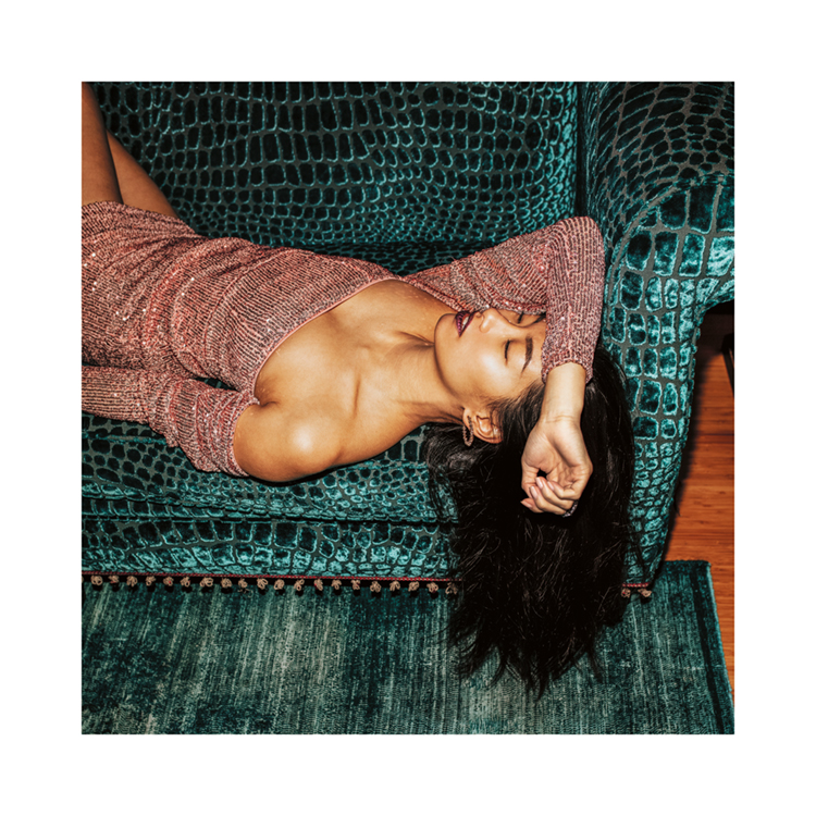  – Fotografía de una mujer con vestido brillante descansando en un sofá turquesa