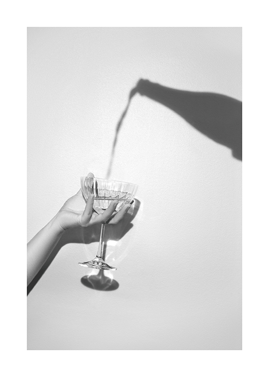  – Fotografía en tonos de gris con la sombra de una botella de champán y una mano con una copa de champán