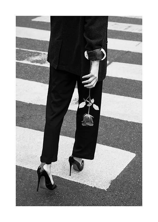  – Fotografía en blanco y negro de una mujer con traje, tacones y una rosa en la mano en un paso de cebra