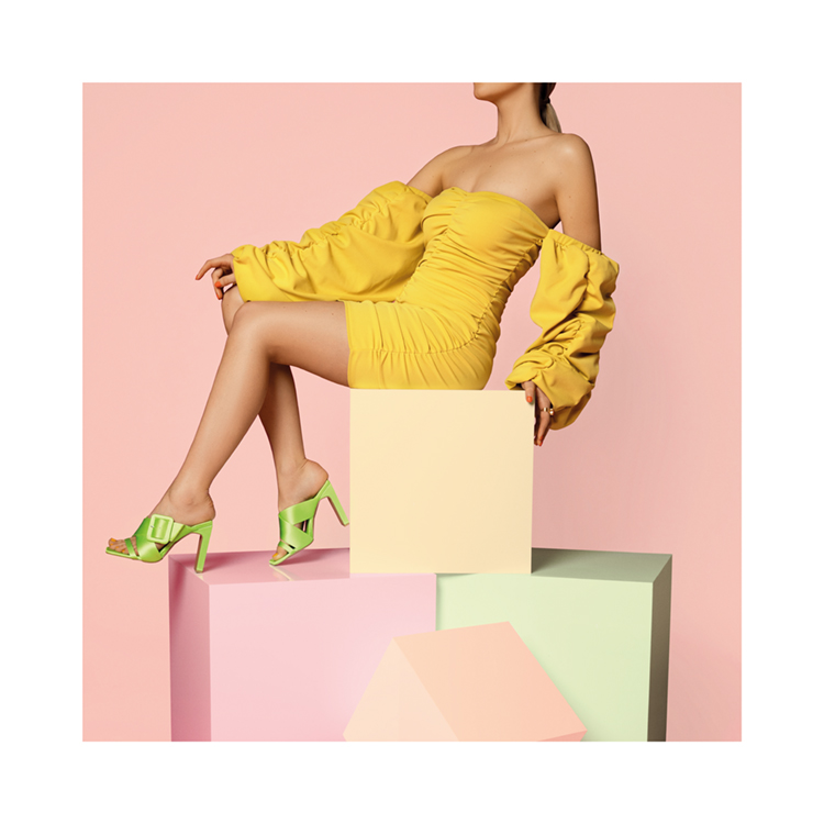  – Mujer con vestido amarillo y tacones verdes sentada sobre una pila de cajas