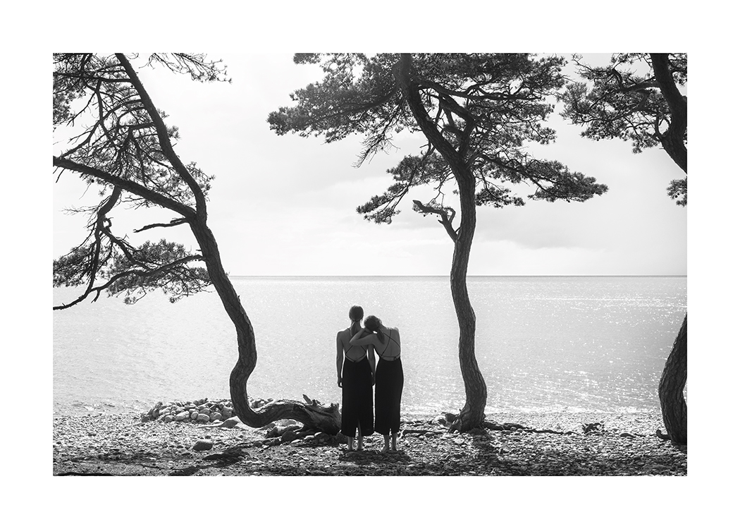  – Fotografía en blanco y negro de dos mujeres en una playa con árboles observando el agua