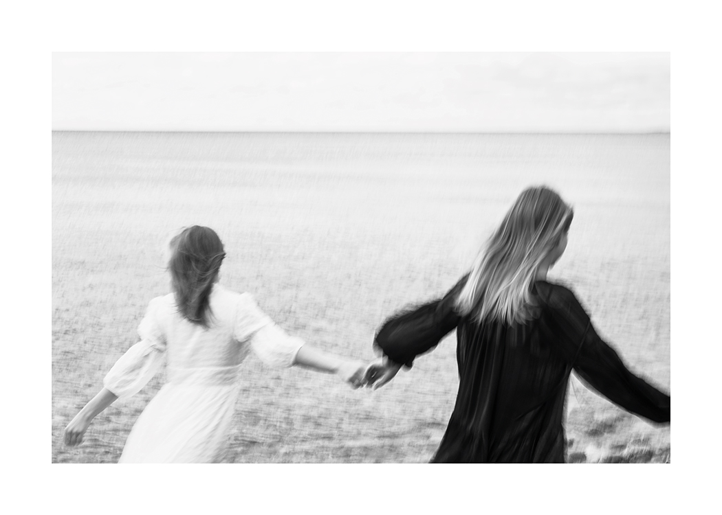  – Fotografía en blanco y negro de dos mujeres corriendo de la mano por un campo