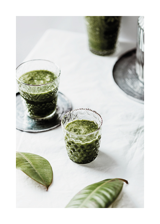  – Fotografía de hojas verdes y vasos con una bebida de color verde apoyados sobre un mantel blanco