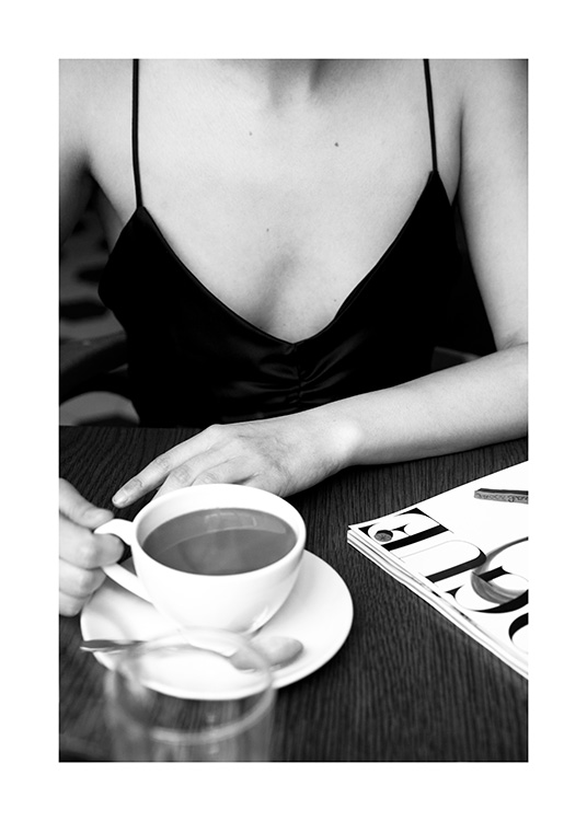  – Fotografía en blanco y negro de una mujer sentada en una cafetería con una taza de café en la mano