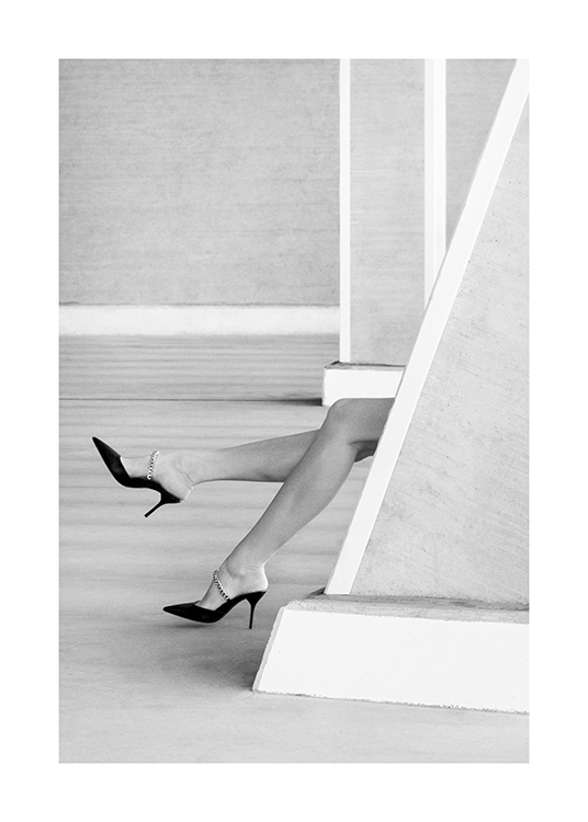 – Fotografía en blanco y negro de dos piernas con zapatos altos asomándose por detrás de un muro