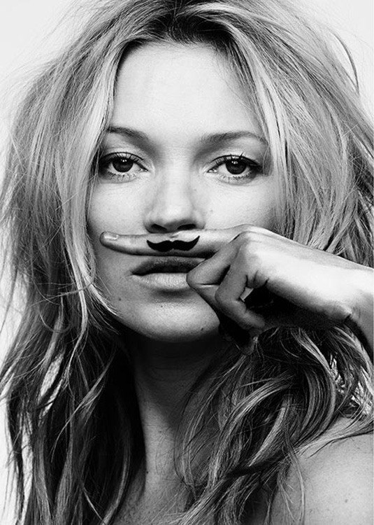  – Fotografía en blanco y negro de Kate Moss con un dedo sobre el labio superior que tiene dibujado un bigote